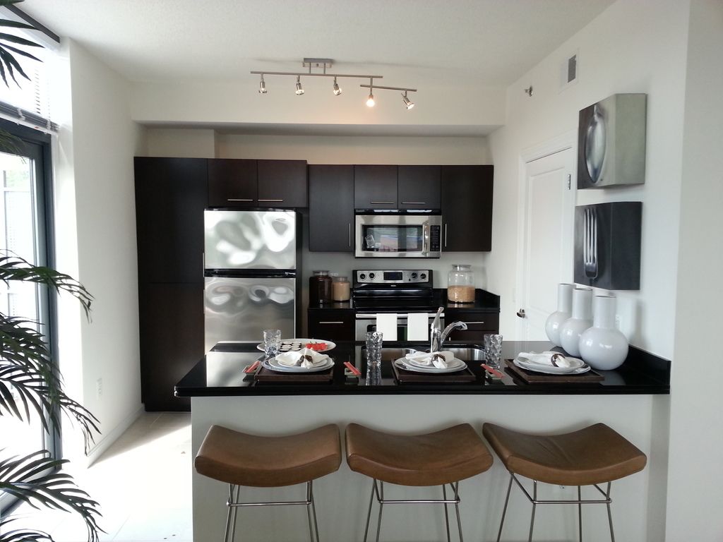 A modern kitchen with dark cabinets, stainless appliances and a breakfast bar with leather stools
