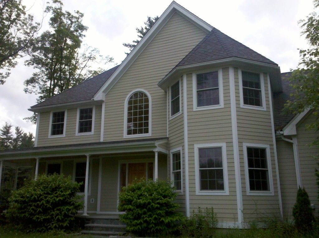 A grey clapboard family home with a turret, arched window and porch among tall trees