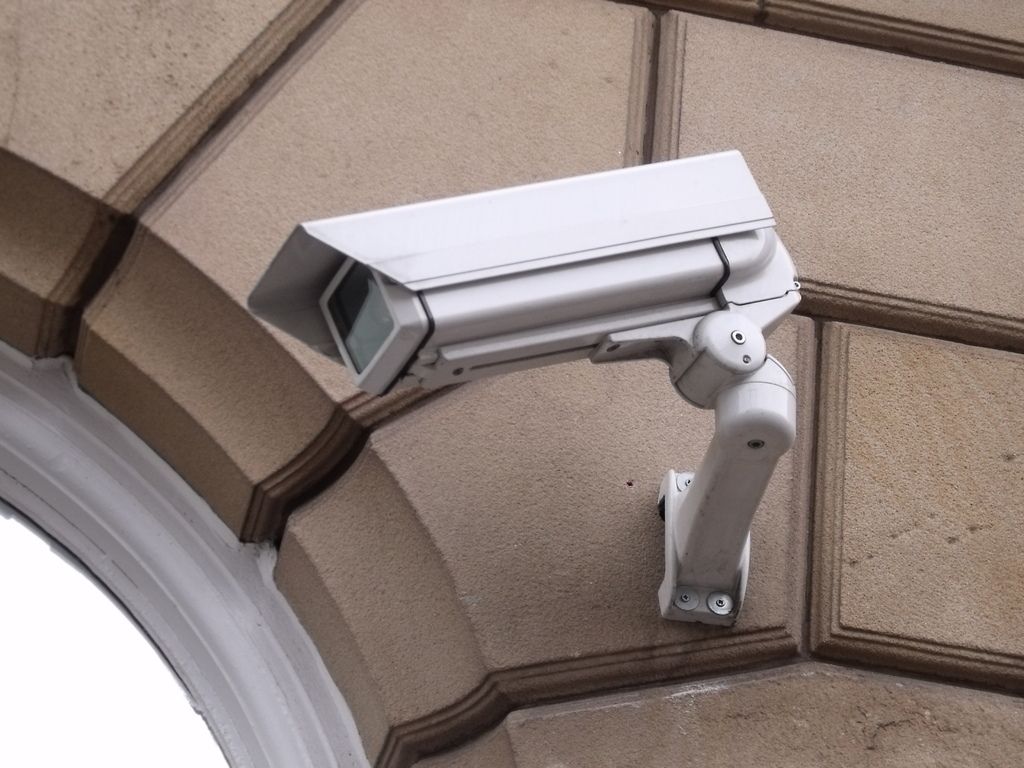A white security camera mounted on the corner of a stone building